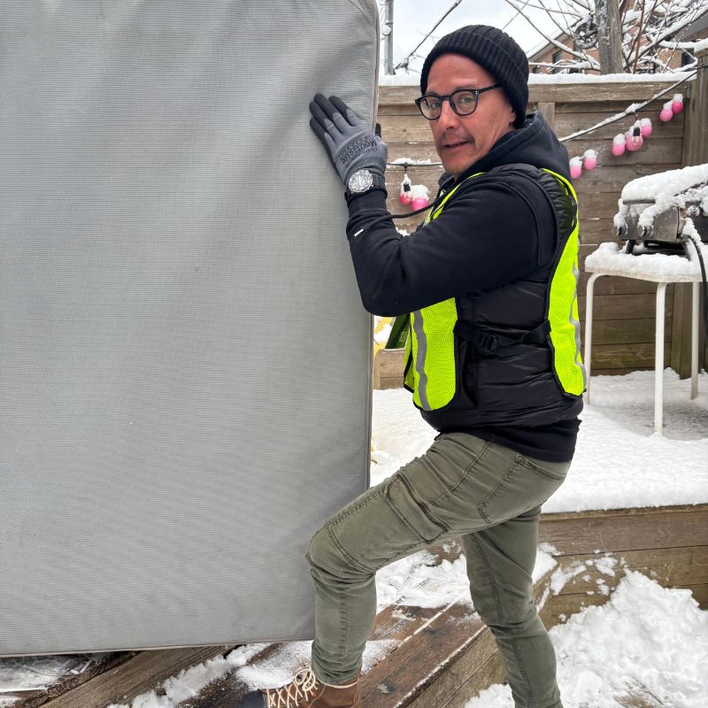 Employé portant un matelas gris sur une terrasse enneigée